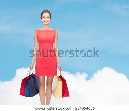 shopping, sale and holidays concept - smiling elegant woman in red dress with shopping bags over blue sky and cloud background over blue sky and cloud background
