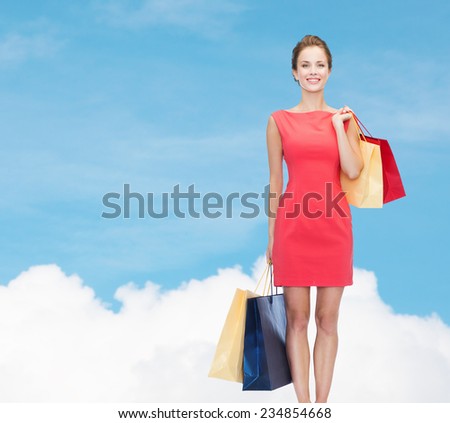 shopping, sale and holidays concept - smiling elegant woman in red dress with shopping bags over blue sky and cloud background over blue sky and cloud background