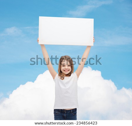 advertisement, childhood, happiness and people concept - smiling little child in white t-shirt holding blank board over blue sky with cloud background