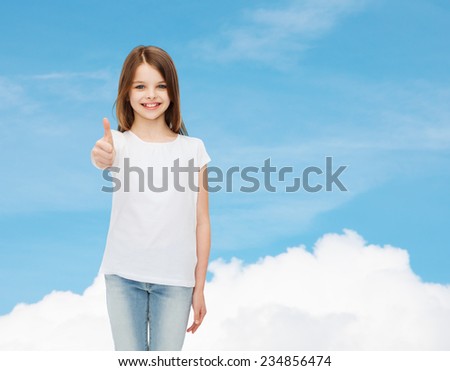 advertising, dream, childhood, gesture and people - smiling little girl in white blank t-shirt showing thumbs up over blue sky background