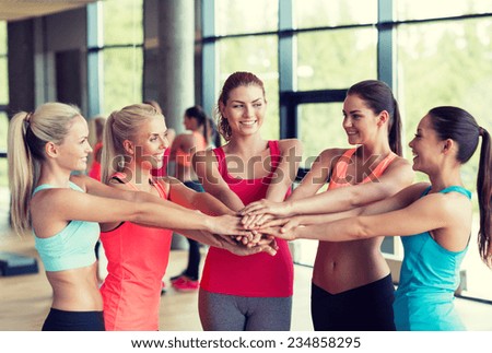 fitness, sport, friendship and lifestyle concept - group of women with hands on top of each other in gym