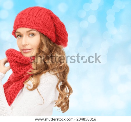 happiness, winter holidays, christmas and people concept - young woman in red hat and scarf over blue lights background