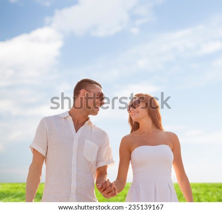 love, people, summer and relations concept - smiling couple wearing sunglasses walking outdoors over blue sky and grass background