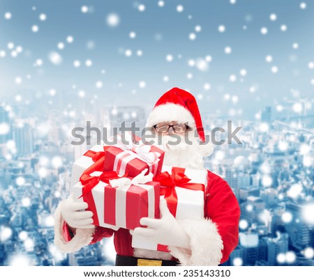 christmas, holidays and people concept - man in costume of santa claus with gift boxes over snowy city background