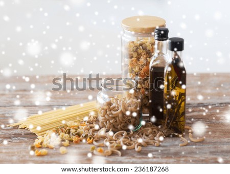 cooking and food concept - close up of two olive oil bottles and pasta in jars on wooden table at home kitchen