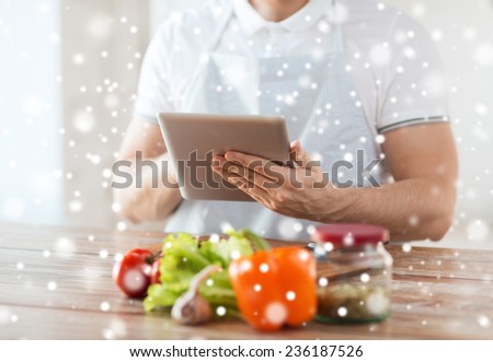 cooking, people, technology and home concept - closeup of man reading recipe from tablet pc computer and vegetables on table in kitchen
