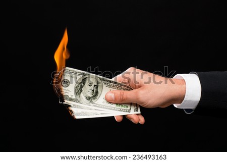 finances, people, savings and bankruptcy concept - close up of male hand holding burning dollar cash money over black background
