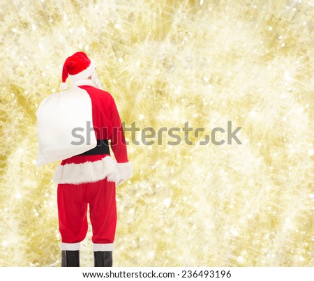 christmas, holidays and people concept - man in costume of santa claus with bag from back over yellow lights background
