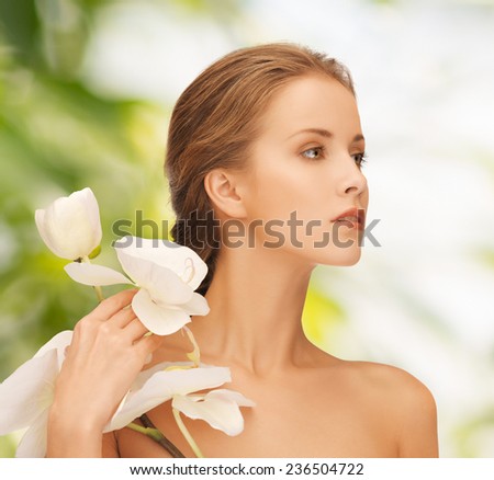 beauty, people and health concept - beautiful young woman with orchid flowers and bare shoulders over green background