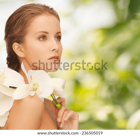 beauty, people and health concept - beautiful young woman with orchid flowers and bare shoulders over green background