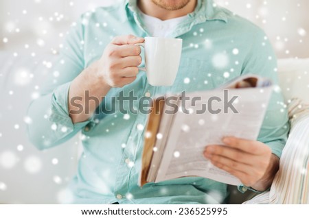 rest, news, drinks and people concept - close up of man reading magazine and drinking from cup sitting on couch at home