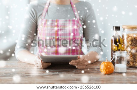 cooking, technology, people and home concept - close up of woman reading recipe from tablet pc computer at kitchen table