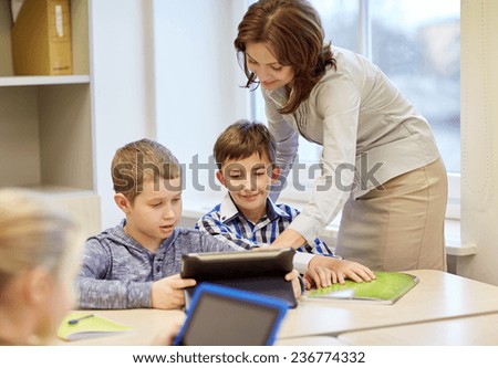 education, elementary school, learning and people concept - teacher helping school kids with tablet pc computer in classroom