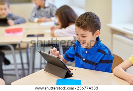 education, elementary school, learning, technology and people concept - little schoolboy with tablet pc computer on break in classroom