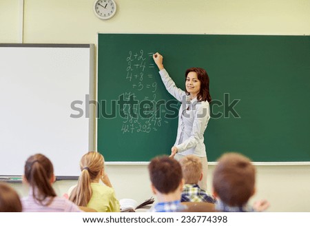 education, elementary, teaching, math and people concept - group of school kids and teacher writing mathematic task on green chalkboard in classroom