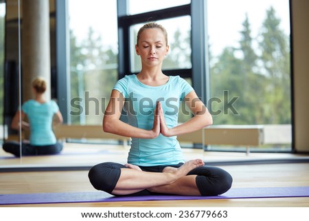fitness, sport, yoga and people concept - happy woman with closed eyes meditating in lotus pose on mat in gym
