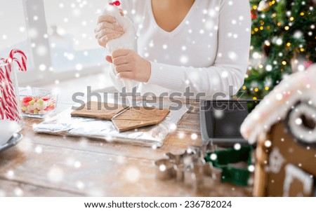 cooking, people, christmas and decoration concept - close up of woman with tablet pc computer making gingerbread houses at home