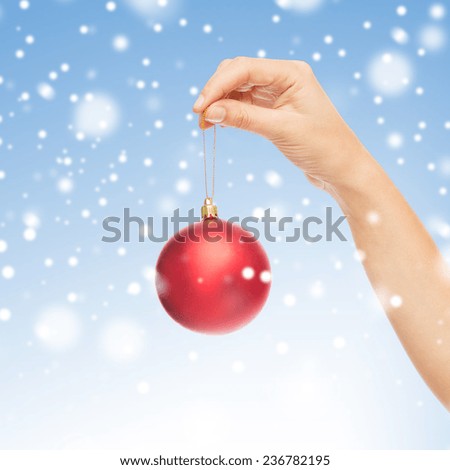 christmas, decoration, holidays and people concept - close up of woman hand holding christmas ball over blue background with snow