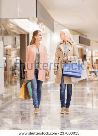 sale, consumerism and people concept - happy young women with shopping bags walking in mall