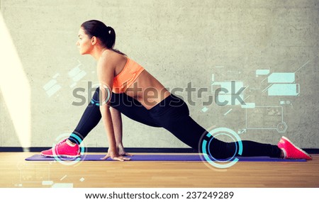 fitness, sport, training, future technology and lifestyle concept - smiling woman stretching leg on mat in gym and projections