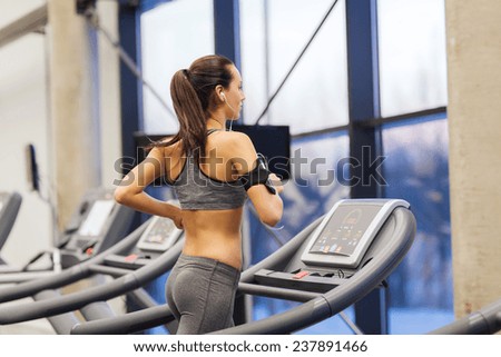 sport, fitness, lifestyle, technology and people concept - woman with smartphone or player and earphones exercising on treadmill in gym