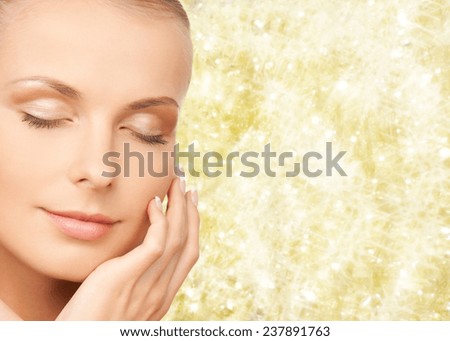 beauty, people and health concept - beautiful young woman touching her face over yellow lights background