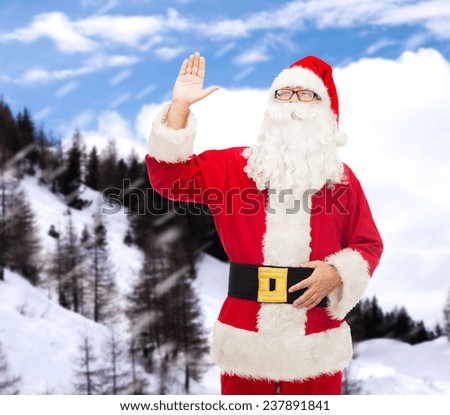 christmas, holidays, gesture and people concept - man in costume of santa claus waving hand over snowy mountains background