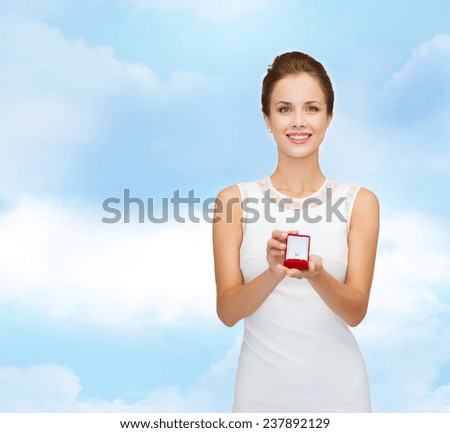 wedding, love, engagement and people concept - smiling woman in white dress holding red gift box with diamond ring over blue cloudy sky background