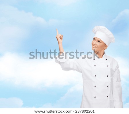 cooking, advertisement and people concept - smiling female chef, cook or baker pointing finger up to something over blue cloudy sky background