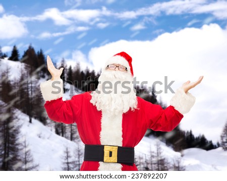 christmas, holidays and people concept - man in costume of santa claus with raised hands over snowy mountains background