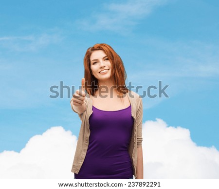 future, dream, gesture and people concept - smiling teenage girl in casual clothes showing thumbs up over blue sky and cloud background
