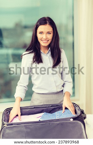 business, technology, internet and hotel concept - happy businesswoman packing things in suitcase in hotel room