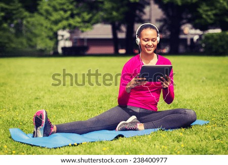 fitness, park, technology and sport concept - smiling african american woman with tablet pc computer and headphones on mat outdoors