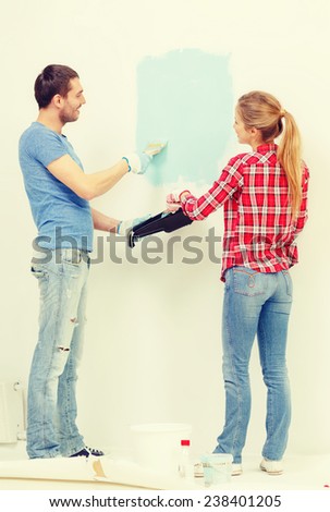 repair, building and home concept - smiling couple painting wall at home