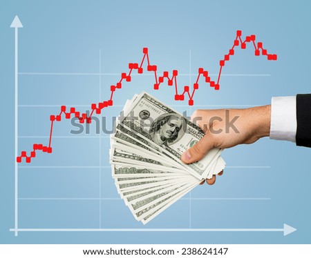 business, finances, people, investments and wealth concept - close up of male stockbroker hand holding dollar cash money over blue background and forex growth chart