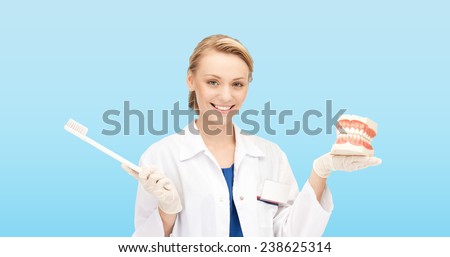 medicine, stomatology, people and hygiene concept - smiling female doctor holding toothbrush and jaws model over blue background