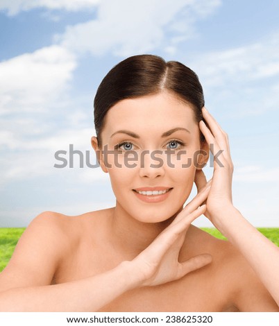 beauty, people and health concept - smiling young woman with bare shoulders over blue sky and grass background