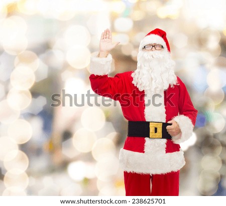 christmas, holidays, gesture and people concept - man in costume of santa claus waving hand over lights background