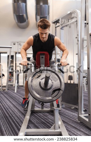 sport, bodybuilding, equipment and people concept - young man with barbell flexing muscles on t-bar row machine in gym