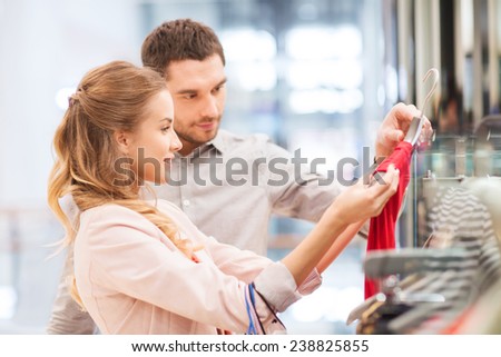 sale, consumerism and people concept - happy young couple with shopping bags choosing dress in mall