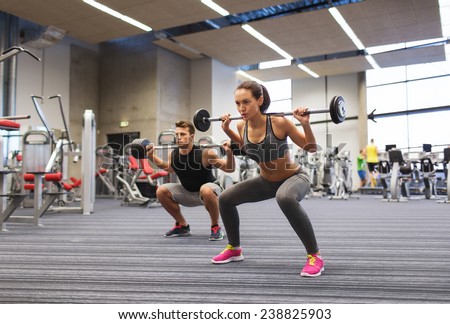 sport, bodybuilding, lifestyle and people concept - young man and woman with barbell flexing muscles and making shoulder press squat in gym