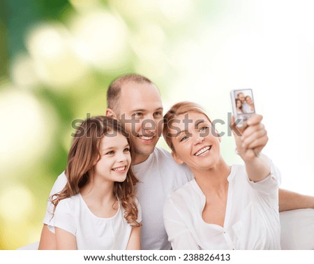 family, technology, ecology and people concept - smiling mother, father and little girl making selfie with camera over green background