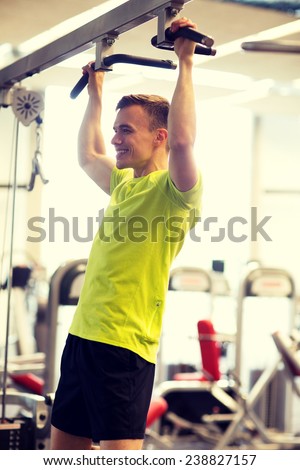 sport, fitness, lifestyle and people concept - smiling man doing pull-ups in gym