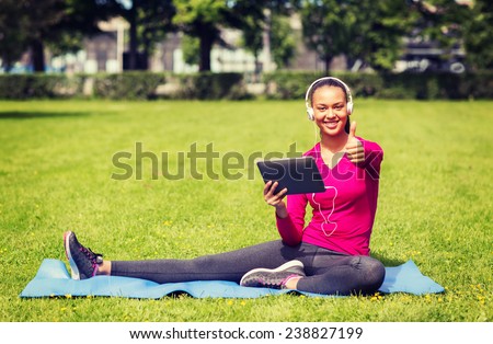 fitness, park, technology and sport concept - smiling african american woman with tablet pc and headphones showing thumbs up outdoors