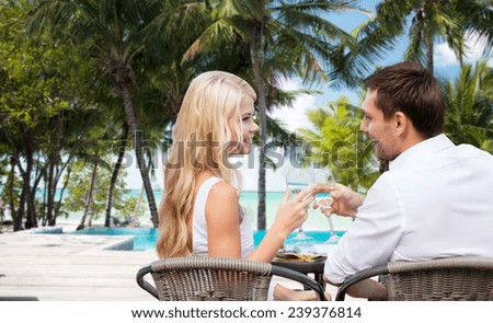 summer holidays, travel, tourism, celebration and dating concept - happy couple drinking wine in cafe over hotel beach with swimming pool background