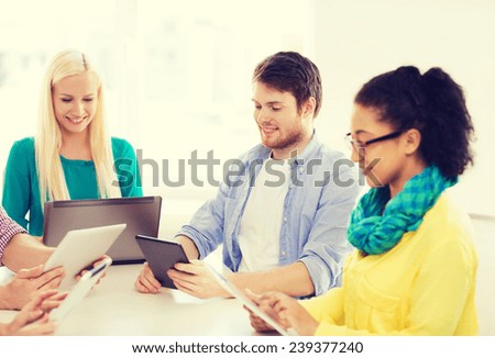 business, office, technology and startup concept - smiling creative team with table pc and laptop computers working in office