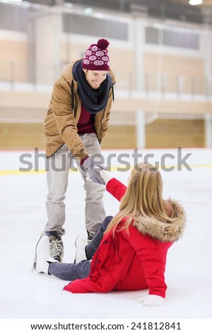 people, friendship, sport and leisure concept - smiling man helping women to rise up on skating rink