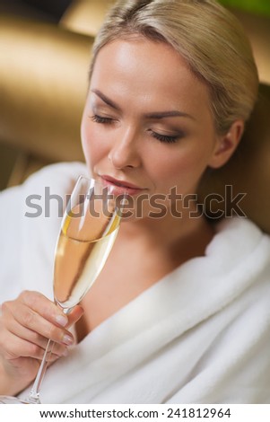 people, beauty, lifestyle, holidays and relaxation concept - beautiful young woman in white bath robe drinking champagne at spa