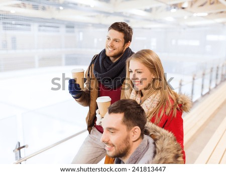 people, friendship, hot drinks and leisure concept - happy friends drinking from paper coffee cups on skating rink