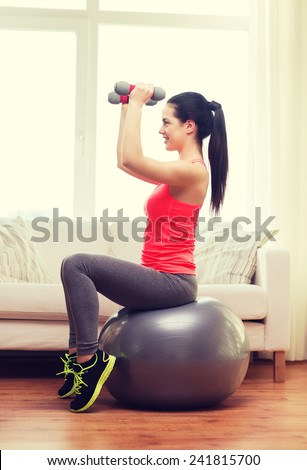 fitness, home and diet concept - smiling girl exercising with fitness ball and dumbbells at home